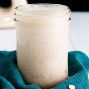 Homemade Vegan Oat Milk in a glass canning jar with a green towel around the bottom