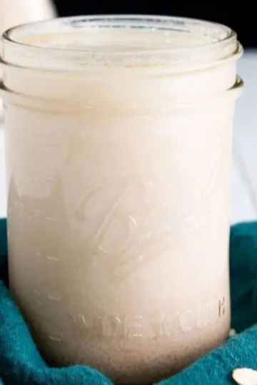 Homemade Vegan Oat Milk in a glass canning jar with a green towel around the bottom