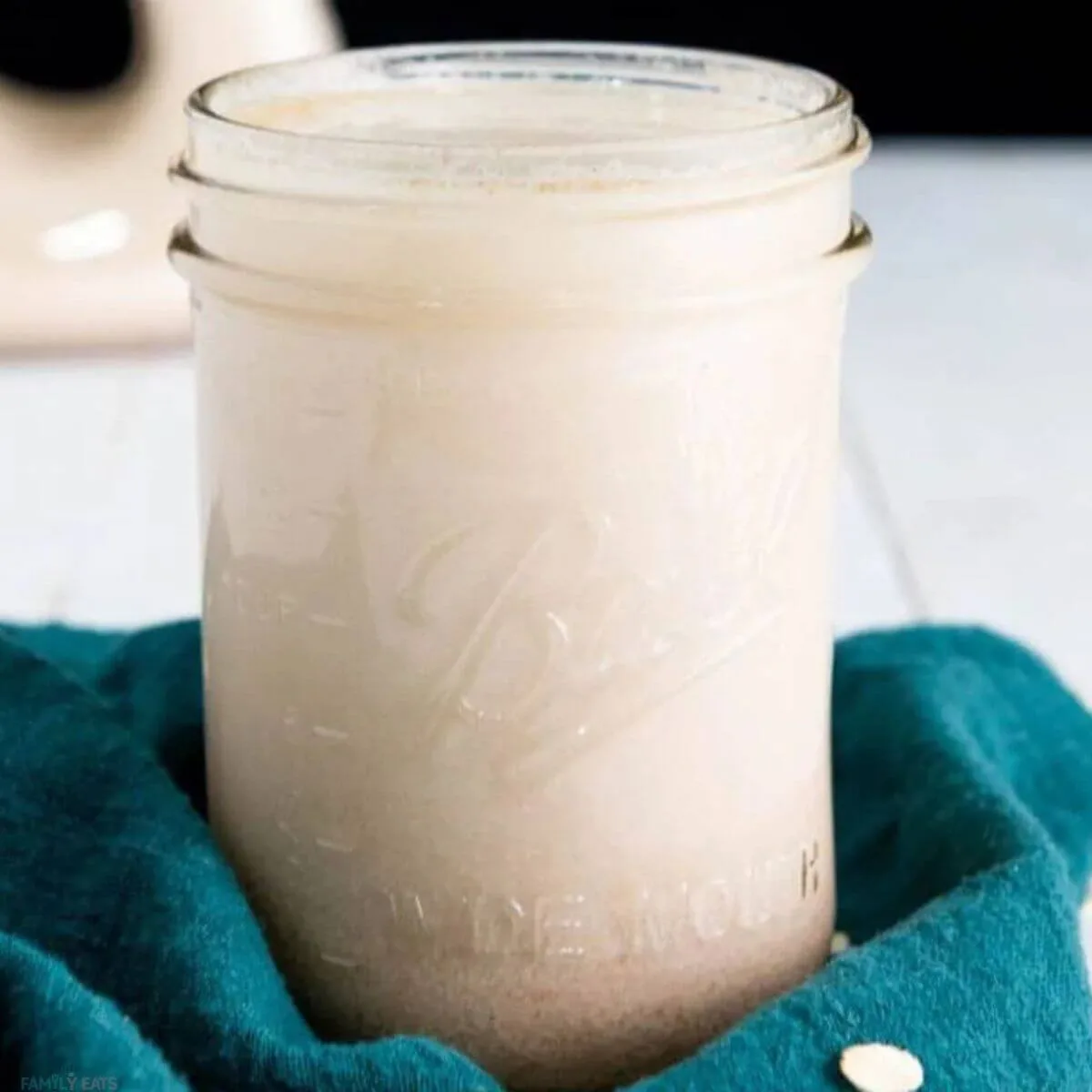 Homemade Vegan Oat Milk in a glass canning jar with a green towel around the bottom