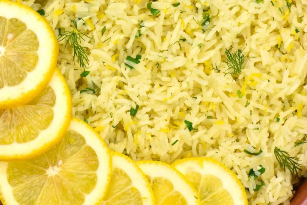 Close-up of cooked rice garnished with finely chopped herbs and lemon zest, with several fresh lemon slices along the bottom edge&mdash;an inviting example of budget friendly rice meals thats both vibrant and satisfying.