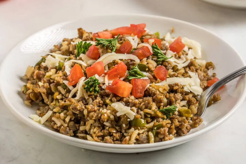 A plate of ground beef and rice topped with shredded cheese, chopped tomatoes, and parsley, with a fork on the side.